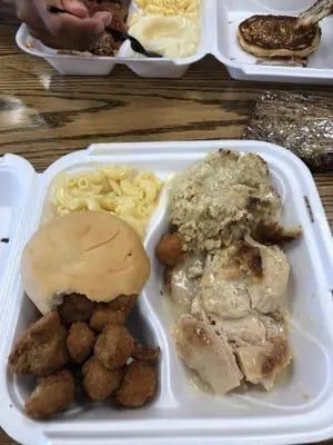 A to-go plate with a roll, a meat and two sides